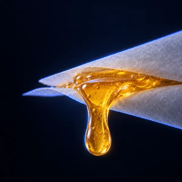 Drop of amber live rosin running between two sheets of baking paper