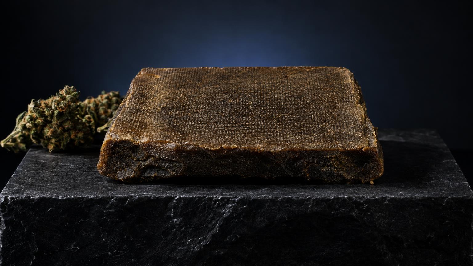Brown compressed brick of Cannabis Resin on black stone with plant material, illustrating concentrated cannabis extract forms
