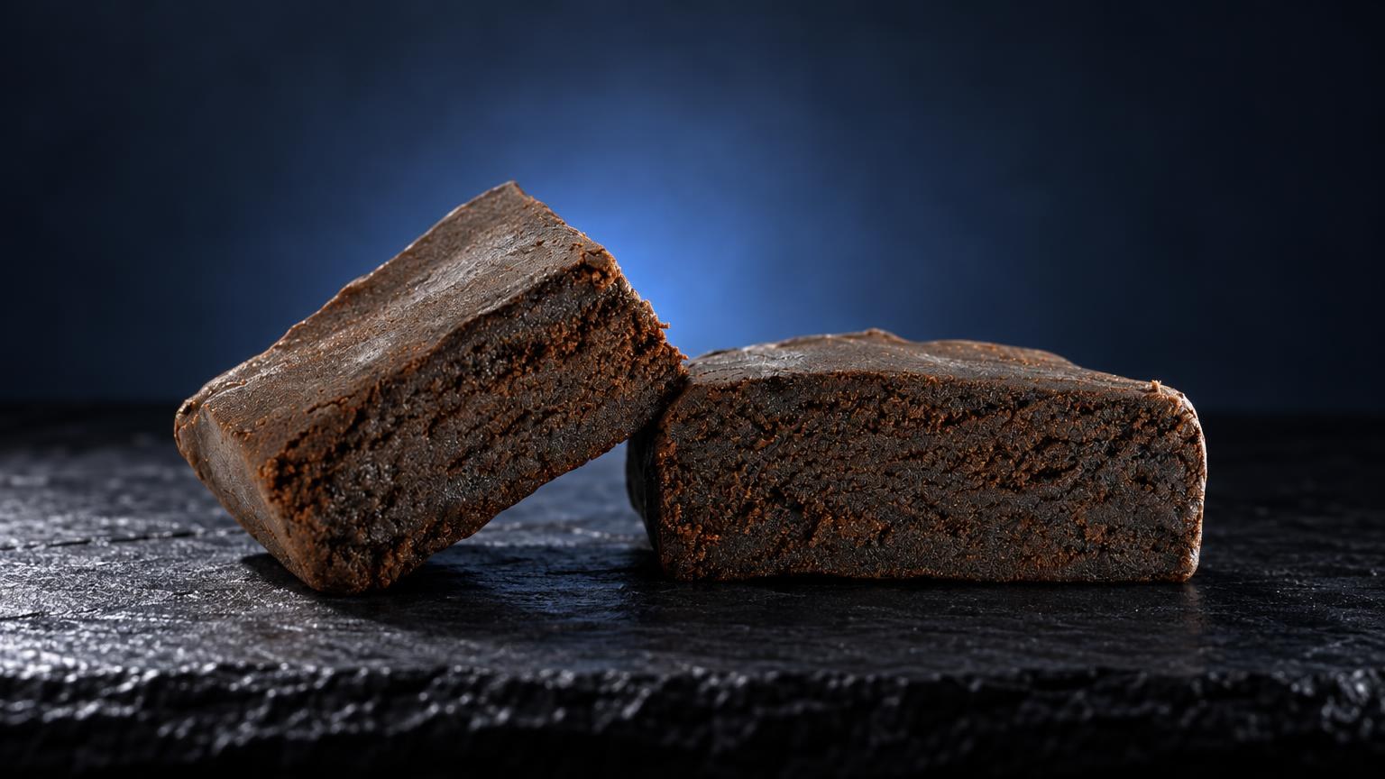 Two dense, brown hash blocks with crumbly texture on dark slate, Hash vs Weed comparison