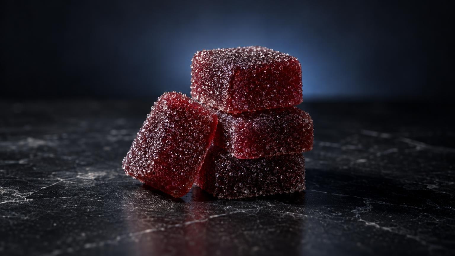 Red sugar-coated gummy candies stacked on dark surface, representing THC Gummies Side Effects topic