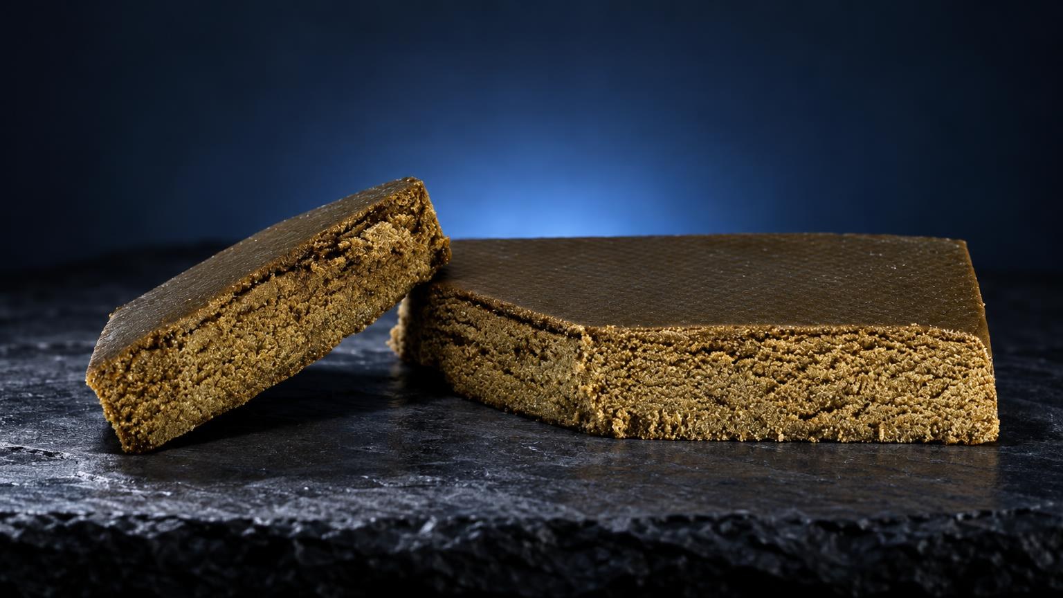 Two blocks of golden-brown Triple Zero with fine, crumbly texture on dark surface, article about triple filtered hash